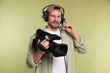 Profesyonel kamera ve soluk zeytinli arka planda kulaklığı olan bir adam.