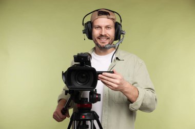 Profesyonel kamera ve soluk zeytinli arka planda kulaklığı olan bir adam.