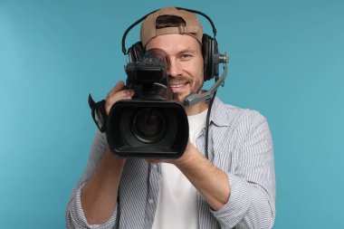 Profesyonel video kamerası ve açık mavi arka planda kulaklığı olan bir adam.