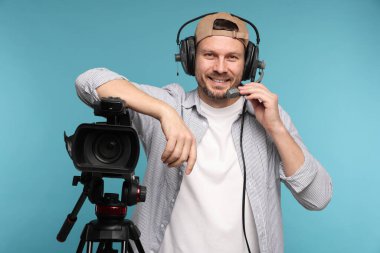 Profesyonel video kamerası ve açık mavi arka planda kulaklığı olan bir adam.
