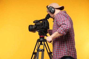 Profesyonel kamera ve turuncu arka planda kulaklığı olan bir adam.