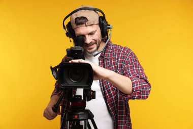 Profesyonel kamera ve turuncu arka planda kulaklığı olan bir adam.