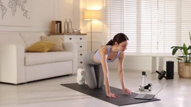 Evde dizüstü bilgisayarla video öğretirken egzersiz yapan kadın.