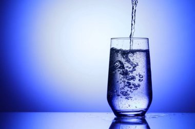 Serinletici gazoz suyunu mavi arka planda cama döküyorum, yakın plan. Metin için boşluk