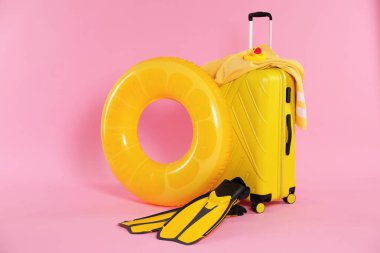 Sarı şişirilebilir yüzük, paletler, bavul, plaj havlusu ve pembe arka planda oyuncak.
