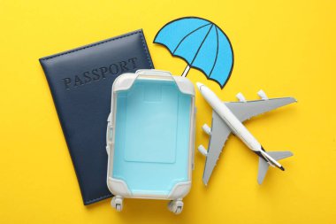 Seyahat sigortası. Uçak modeli, pasaport, kağıt şemsiye ve sarı arka planda bavul.