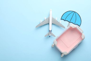 Seyahat sigortası. Uçak modeli, kağıt şemsiye ve açık mavi arka planda bavul, düz. Metin için boşluk