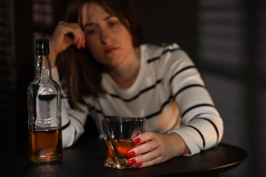 Alkol bağımlılığı. İçerideki masada bir bardak viski ve şişe taşıyan bir kadın. Seçici bir odak noktası.