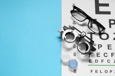 Gözlükler, deneme çerçevesi, görüş testi çizelgesi ve açık mavi arka planda lensler, düz konum. Metin için boşluk