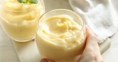 Beyaz ahşap masada nefis vanilyalı puding yiyen bir kadın.