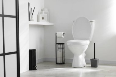 Tuvalet, fırça ve ihtiyaçlar banyoda beyaz duvarın yanında.