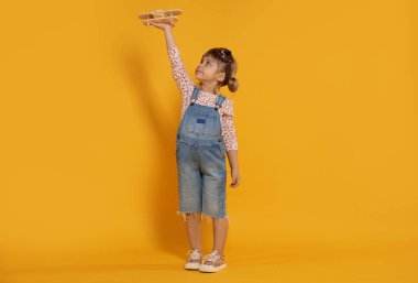 Turuncu arka planda oyuncak uçakla oynayan sevimli küçük kız.