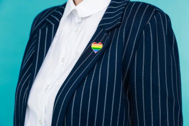 Açık mavi arkaplanda LGBT renginde kalp şeklinde iğnesi olan kadın, yakın plan