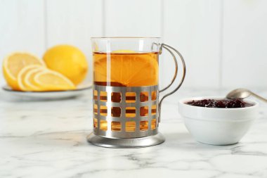 Metal tutacakta bir bardak çay, reçel ve limon dilimleri beyaz mermer masada, yakın plan.