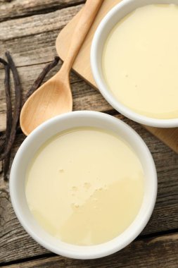 Yoğun süt, kaşık ve vanilya kapsülleri ahşap masada, düz yerde.