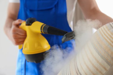 Temizlikçi yastığı evde buhar temizleyicisiyle temizliyor.