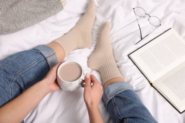Bir fincan sıcak içecekle yatakta bej çorap giyen bir kadın, yakın plan.