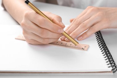 Beyaz masadaki deftere cetvel ve kalemle çizim yapan kadın, yakın plan.