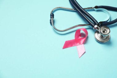 Göğüs kanseri farkındalığı. Açık mavi arka planda pembe kurdele ve steteskop. Metin için boşluk