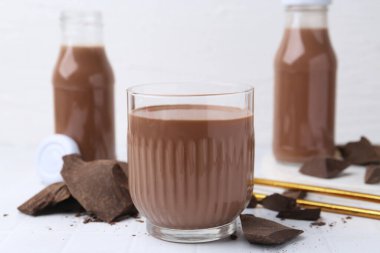 Bardakta çikolatalı süt ve beyaz fayanslı masada çikolata parçaları, yakın plan.