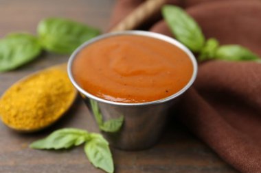 Lezzetli köri sosu metal tabakta, toz ve fesleğen ahşap masada, yakın plan.