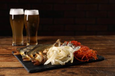 Different dried fish snacks and beer on wooden table. Space for text