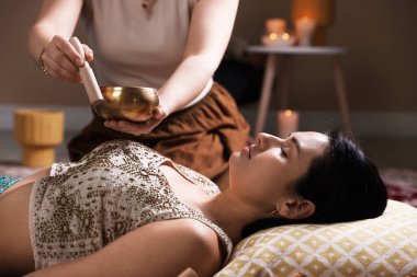 Şarkı söyleyen kadın kase terapisi görüyor. Kapalı yerde yatıyor.