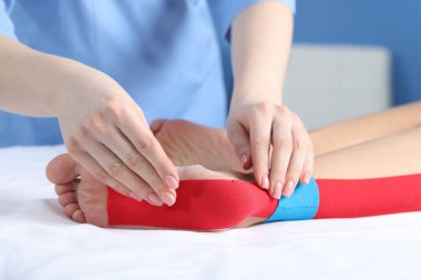 Hastanedeki hastanın ayağına Kinesio bantları takan doktor.
