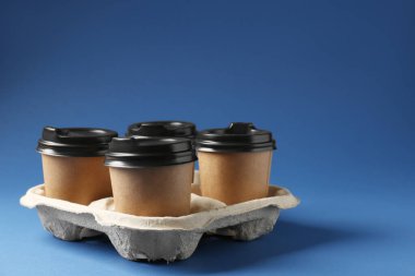 Kağıt kahve bardakları mavi arka planda karton tutacakta. Metin için boşluk