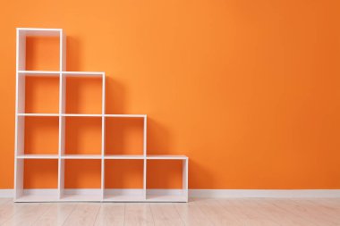 Empty shelving unit near orange wall indoors. Space for text