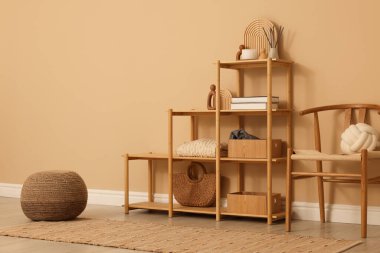 İçerideki bej duvarın yanında dekor, sandalye ve puf bulunan raf ünitesi.