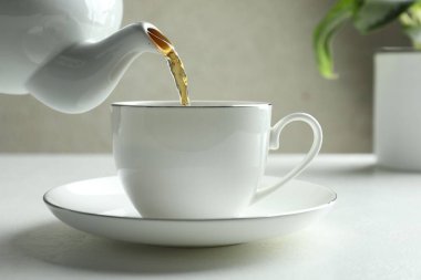 Beyaz masada çaydanlıktan fincana taze demlenmiş çay dökülüyor, yakın plan.