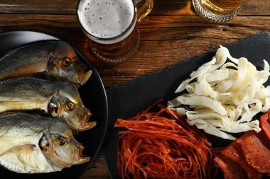 Kurutulmuş balık atıştırmalıkları ve bira ahşap masada, düz yatıyordu.