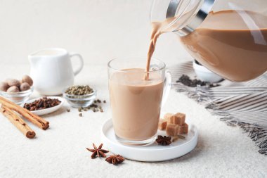 Beyaz desenli masada cam fincana aromatik Masala çayı dökülüyor, yakın plan.