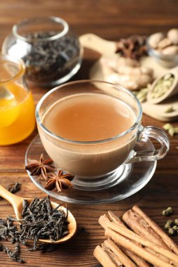 Aromatik Masala çayı fincanda, baharatlar, kuru yapraklar ve bal ahşap masada, yakın plan.