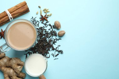 Cam fincanda Aromatik Masala çayı, baharatlar, kuru yapraklar ve açık mavi arka planda süt. Metin için boşluk