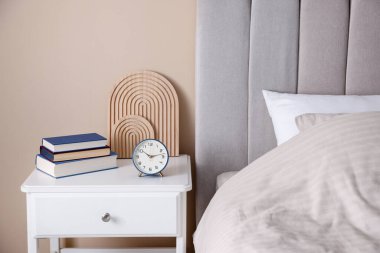Yatağın yanında kitap, dekor ve alarmlı bir masa var.