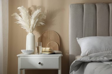 Yatağın yanında kitap, dekor ve bir bardak su olan komodin.