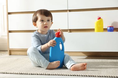 Evdeki dolabın yanında deterjan şişeleriyle oynayan küçük bir çocuk. Çocuk tehlikede.