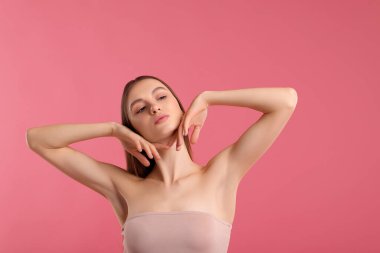 Pembe arka plandaki epilasyondan sonra pürüzsüz bir ten gösteren genç kadın.