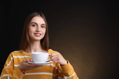 Kahverengi arka planda bir fincan kahveyle gülümseyen kadın. Metin için boşluk