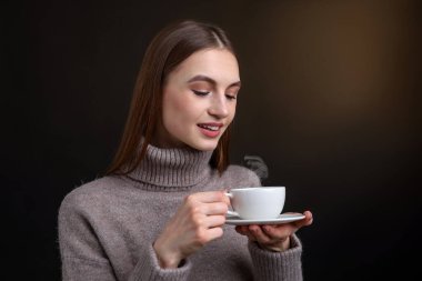 Kahverengi arka planda bir fincan kahveyle gülümseyen kadın.