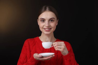 Kahverengi arka planda bir fincan kahveyle gülümseyen kadın.