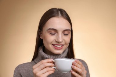 Bej renkli arka planda bir fincan kahveyle gülümseyen kadın