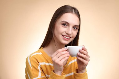 Bej renkli arka planda bir fincan kahveyle gülümseyen kadın