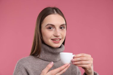 Pembe arka planda bir fincan kahveyle gülümseyen kadın.