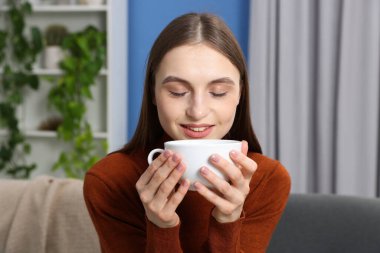 Evdeki kanepede bir fincan kahveyle gülümseyen kadın.