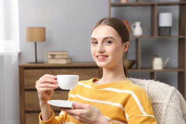 Evde bir fincan kahveyle gülümseyen kadın.