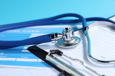 Açık mavi arkaplanda stetoskop ve sağlık kartı formları, yakın plan.