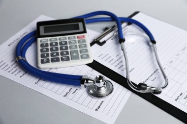 Stetoskop, tıbbi kart formları ve gri arka planda hesap makinesi, yakın plan.